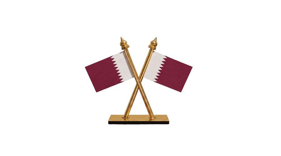 Two crossed Qatar car flags on a rectangular gilt stand.