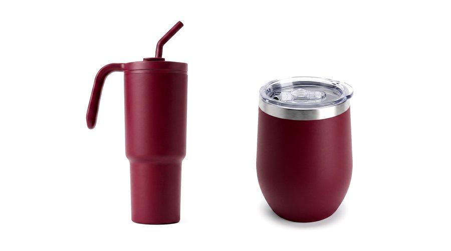 A maroon tumbler with a handle and straw beside a stemless maroon cup.