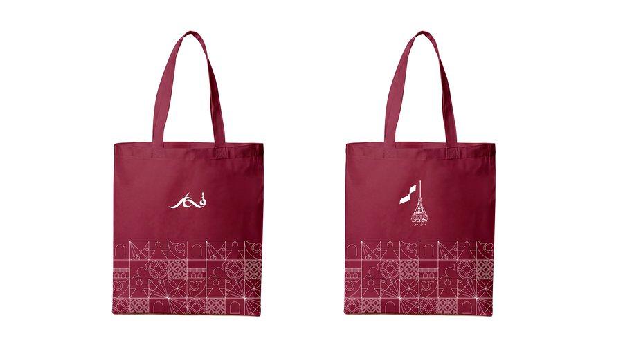 The maroon National Day tote bag, front and back, with calligraphy and a heritage tile band.