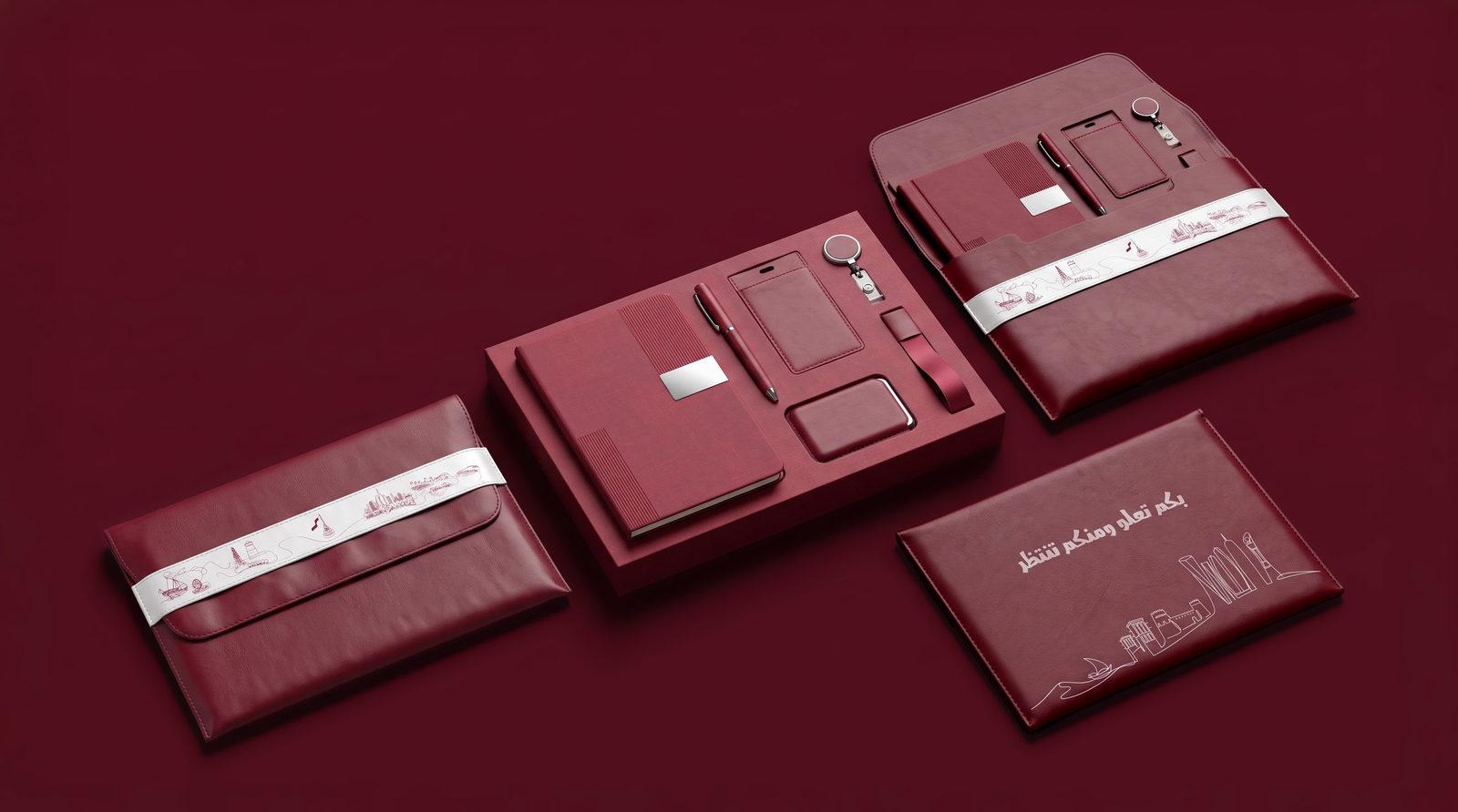 The Huwiyyat Watan employee set laid out on deep maroon: leather sleeve, notebook, pen, ID holder and badge reel.